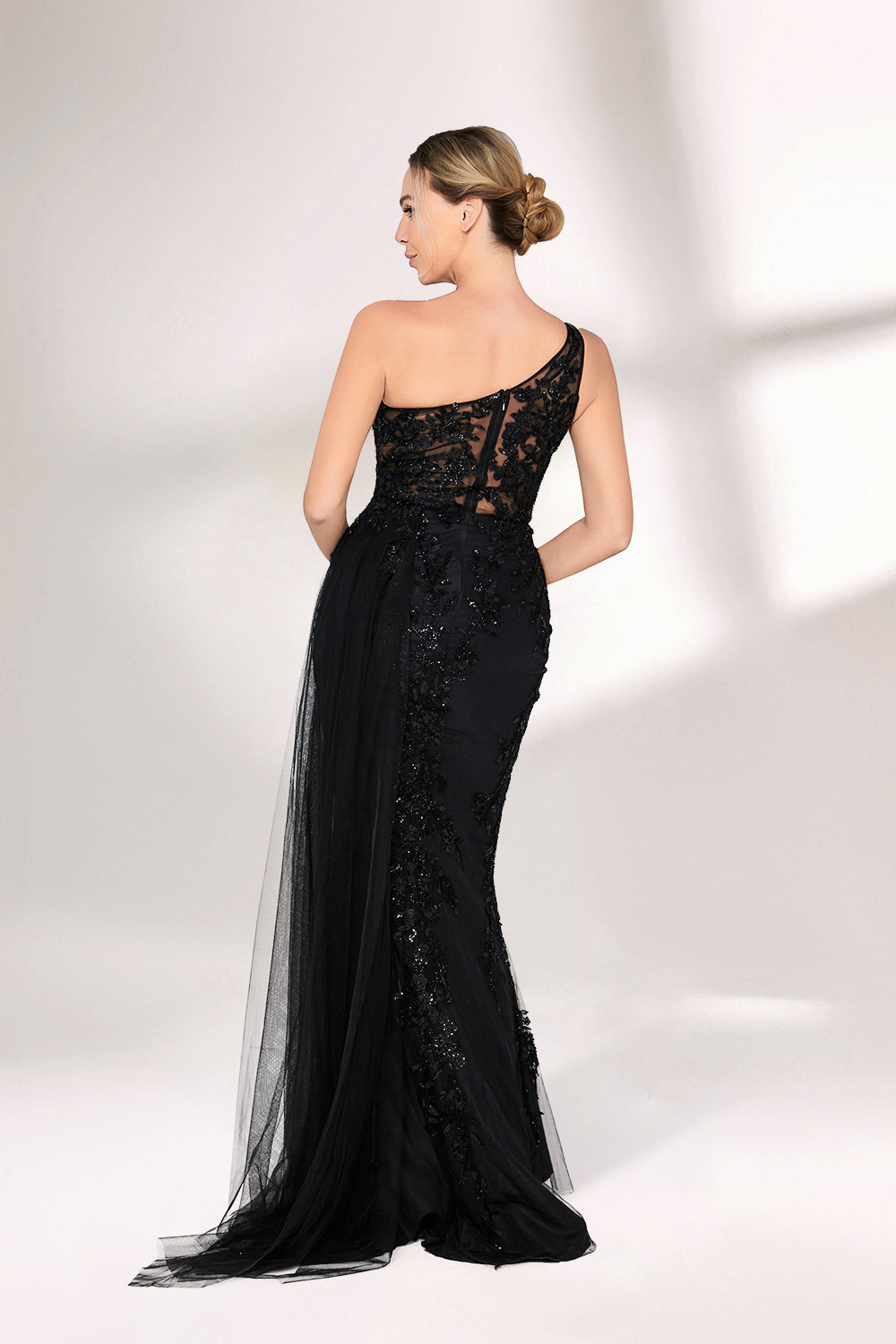 A woman dons a stunning black one - shoulder evening gown. The bodice is intricately adorned with beadwork and embroidery, adding a touch of luxury. The dress has a form - fitting silhouette that hugs the curves, and a high side slit reveals a hint of leg. A sheer, flowing overlay cascades down from the side, enhancing the gown's elegance. Paired with simple strappy silver heels, she stands gracefully against a light - colored backdrop, making the dress perfect for formal galas or upscale events.02