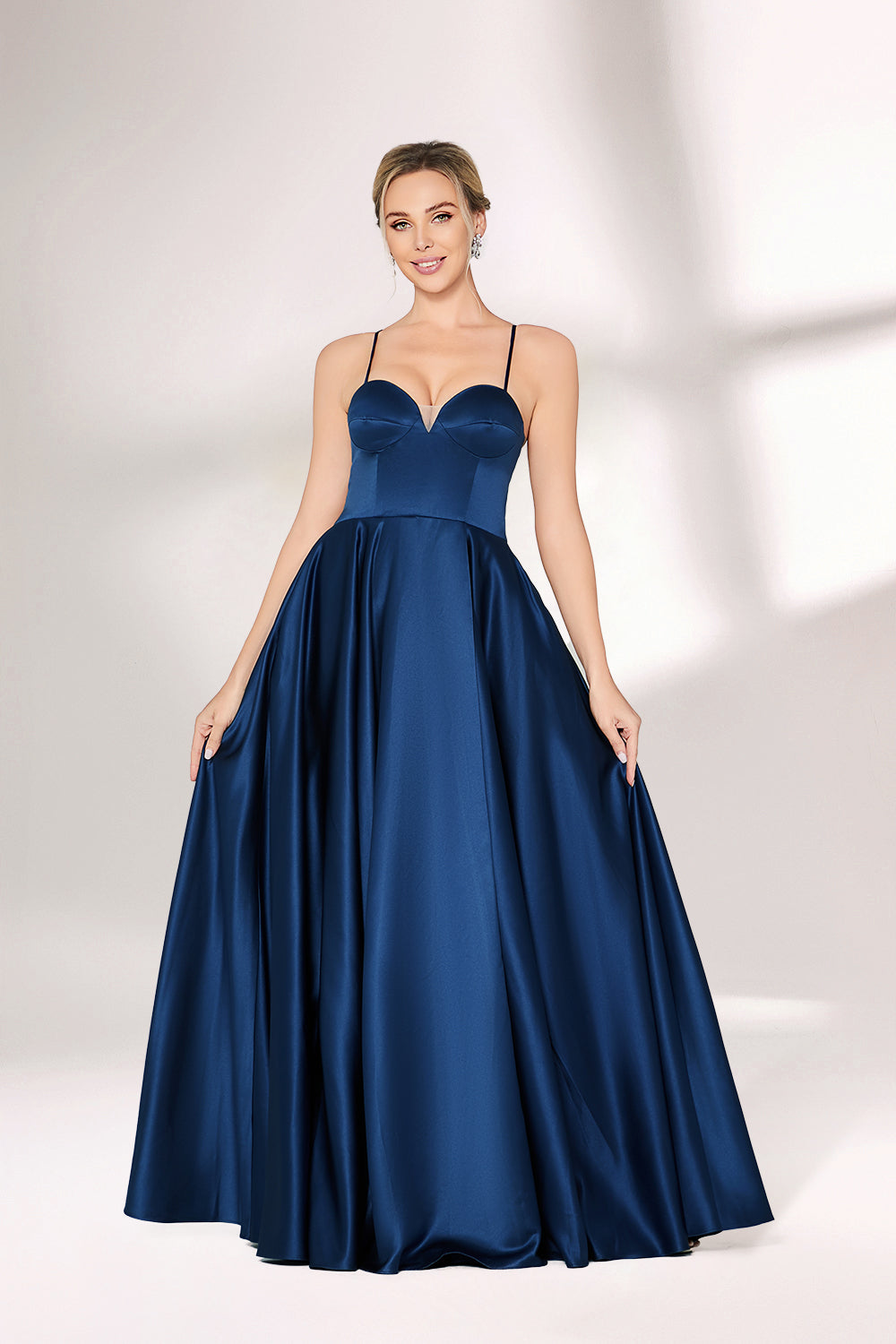 A woman with short, sleek hair and a poised demeanor wears a navy - blue satin gown. It has thin spaghetti straps, a sweetheart neckline, and a voluminous, flowing skirt. Paired with understated heels, the outfit radiates elegance, ideal for formal events like galas or weddings.03