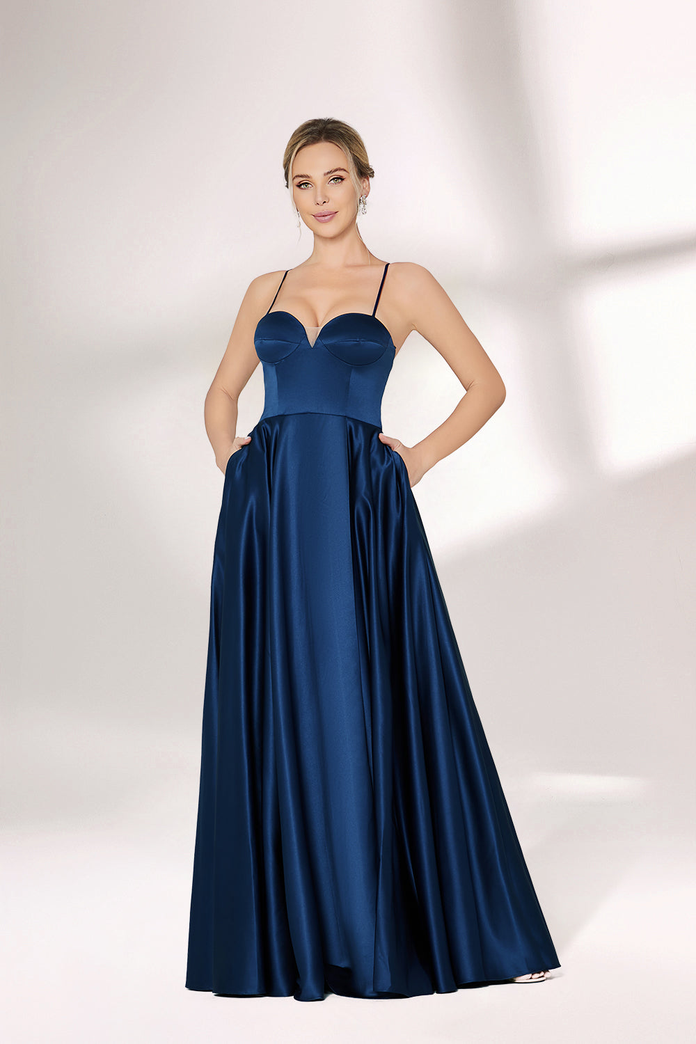 A woman with short, sleek hair and a poised demeanor wears a navy - blue satin gown. It has thin spaghetti straps, a sweetheart neckline, and a voluminous, flowing skirt. Paired with understated heels, the outfit radiates elegance, ideal for formal events like galas or weddings.01