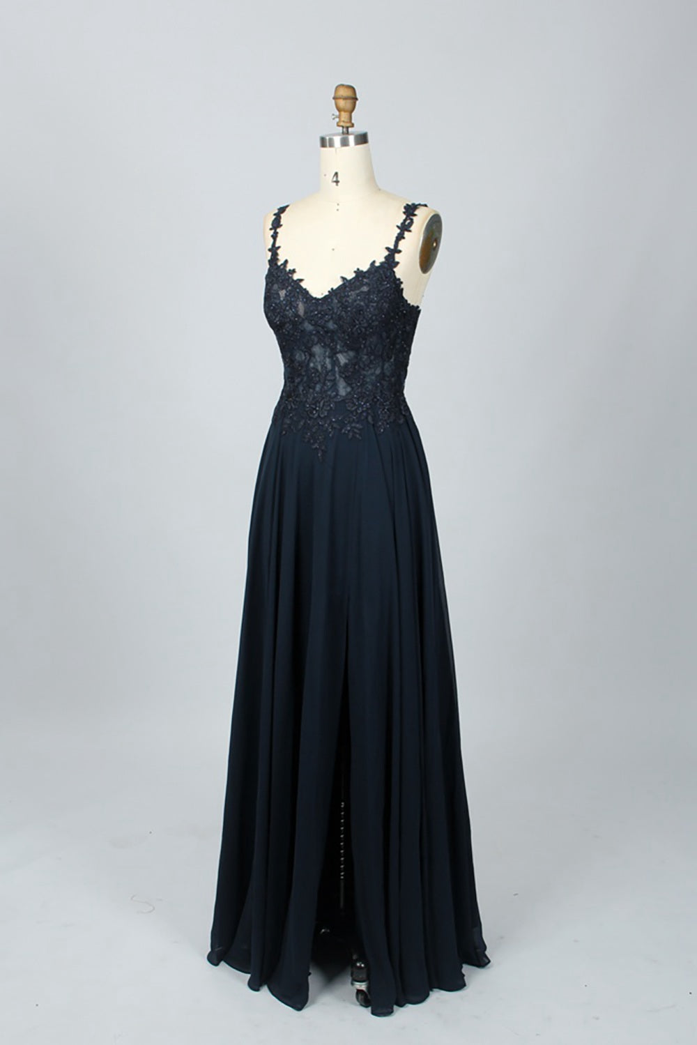 Photograph of a blue, floor-length, sleeveless gown with intricate lace detailing on the bodice and a subtle thigh-high slit, displayed on a mannequin. The gown has a fitted top and a flowing, soft fabric skirt. The background is plain beige.08