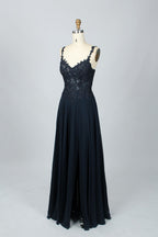 Photograph of a blue, floor-length, sleeveless gown with intricate lace detailing on the bodice and a subtle thigh-high slit, displayed on a mannequin. The gown has a fitted top and a flowing, soft fabric skirt. The background is plain beige.08