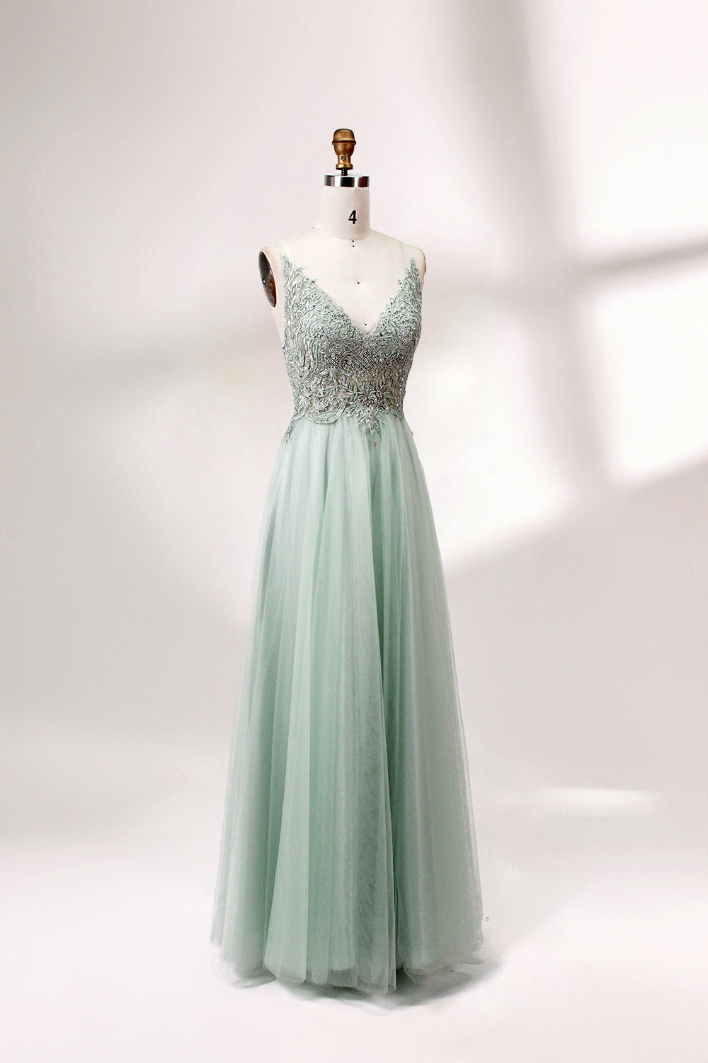 A mannequin showcases a light - green tulle gown with a lace - embroidered, sheer bodice. It has thin straps, a deep V - neckline, and a voluminous skirt. The delicate lace and flowing tulle create a romantic look, perfect for formal events like weddings or proms, exuding elegance.
3