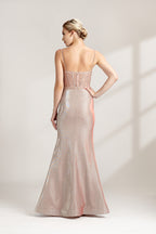 A photograph of a slender, fair-skinned woman with short blonde hair, wearing a floor-length, shimmering silver gown with a lace bodice and spaghetti straps. She stands confidently against a plain white background with soft, diffused light casting subtle shadows. The gown features a flattering, form-fitting silhouette.32547-02