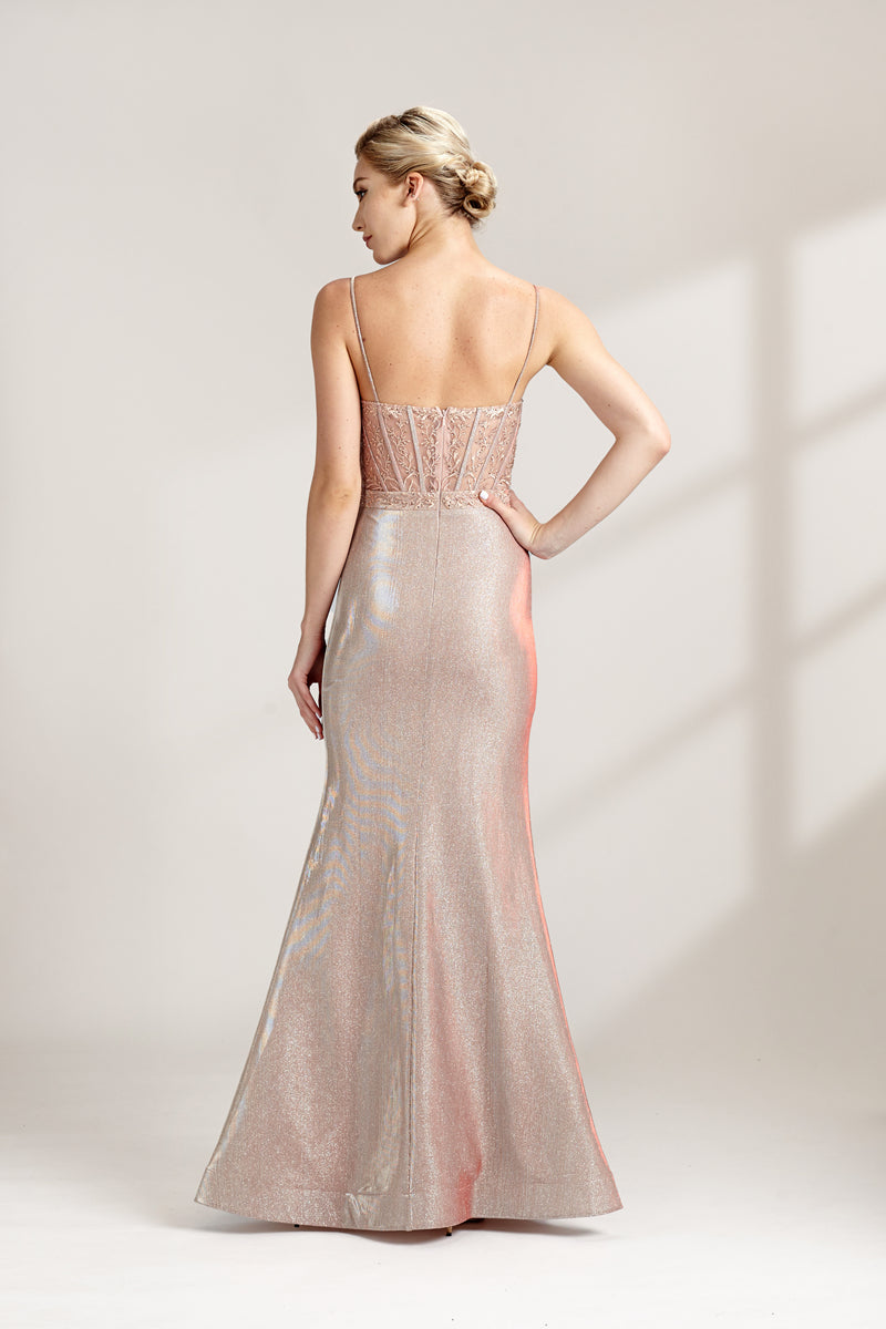 A photograph of a slender, fair-skinned woman with short blonde hair, wearing a floor-length, shimmering silver gown with a lace bodice and spaghetti straps. She stands confidently against a plain white background with soft, diffused light casting subtle shadows. The gown features a flattering, form-fitting silhouette.32547-02