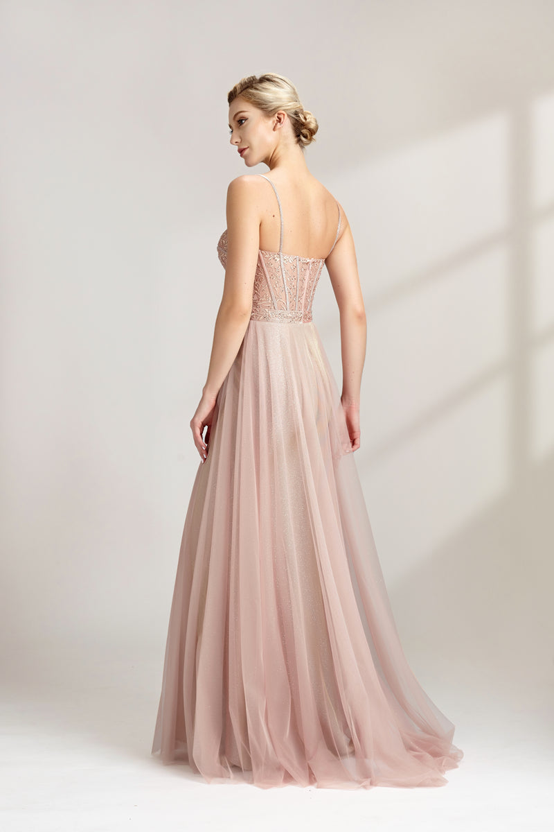 Photograph of a slim, fair-skinned woman with short blonde hair styled in a sleek updo. She wears a floor-length, light pink, sheer tulle gown with intricate lace detailing on the bodice. The gown has spaghetti straps and a sweetheart neckline. She stands against a plain white background, casting soft shadows. The overall aesthetic is elegant and sophisticated.32547b.03