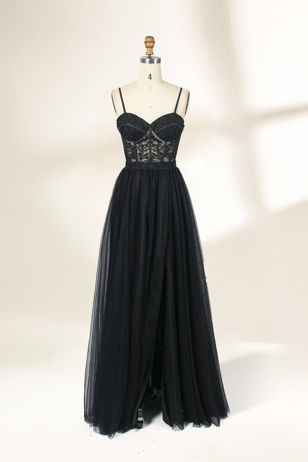 Photograph of a black, lace-trimmed, strapless gown with a sweetheart neckline and a full, flowing tulle skirt. The dress is displayed on a white mannequin with a wooden stand against a plain, light beige background, creating a simple and elegant setting.32547c-2.1
