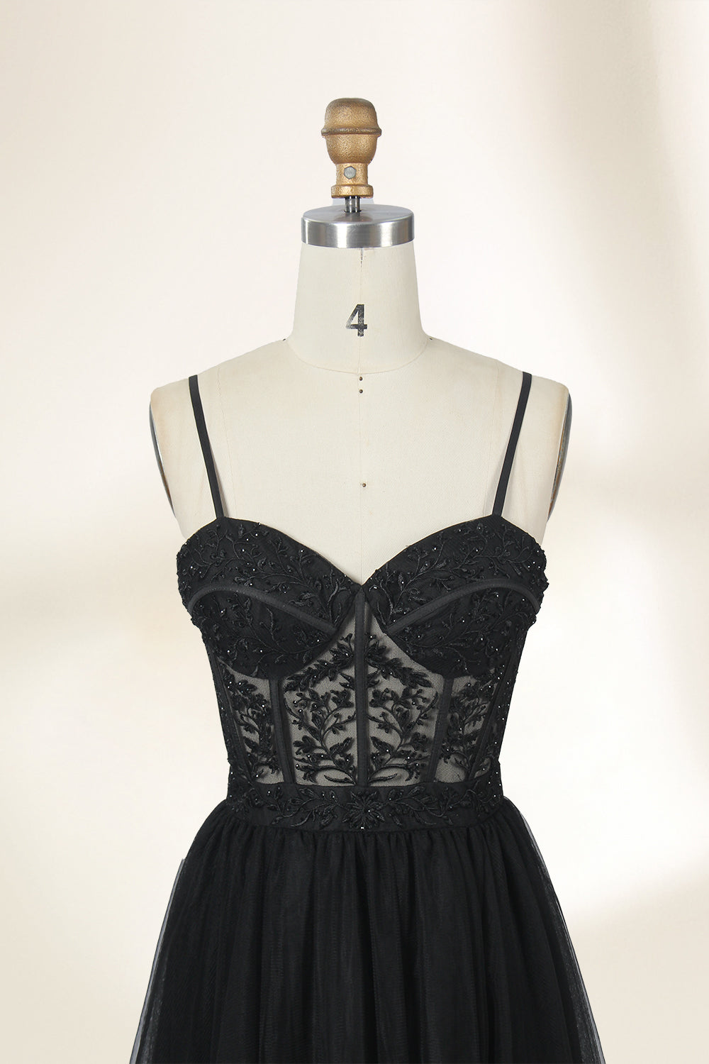 Photograph of a black, lace-trimmed, strapless gown with a sweetheart neckline and a full, flowing tulle skirt. The dress is displayed on a white mannequin with a wooden stand against a plain, light beige background, creating a simple and elegant setting.32547c-2.3