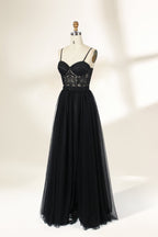 Photograph of a black, lace-trimmed, strapless gown with a sweetheart neckline and a full, flowing tulle skirt. The dress is displayed on a white mannequin with a wooden stand against a plain, light beige background, creating a simple and elegant setting.32547c-2.5