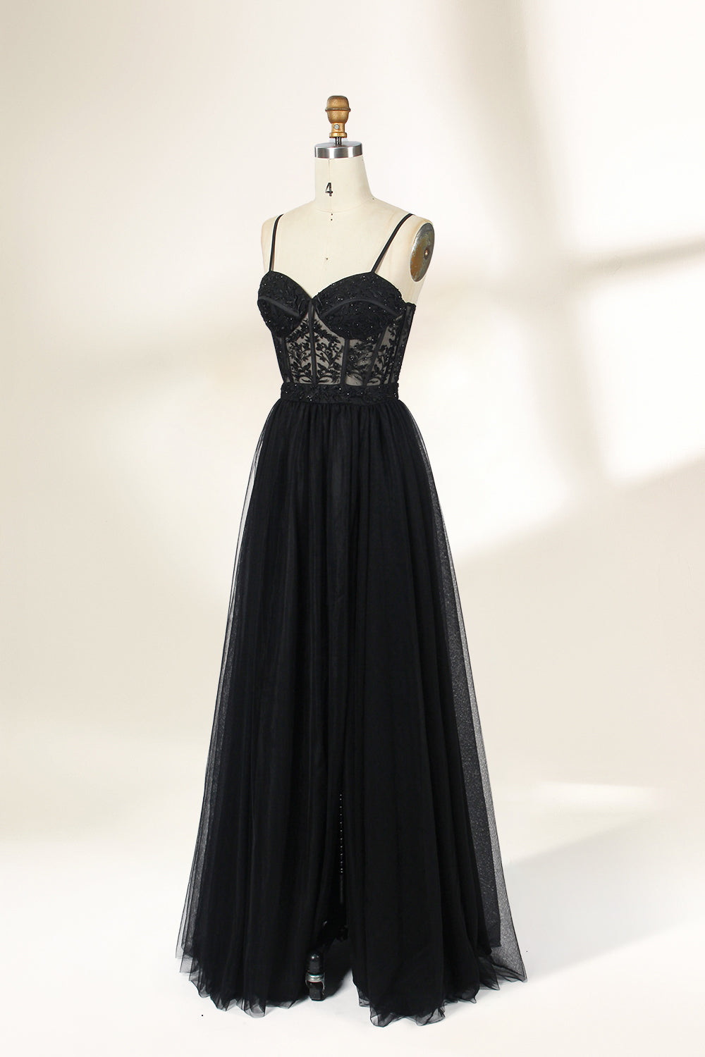 Photograph of a black, lace-trimmed, strapless gown with a sweetheart neckline and a full, flowing tulle skirt. The dress is displayed on a white mannequin with a wooden stand against a plain, light beige background, creating a simple and elegant setting.32547c-2.5