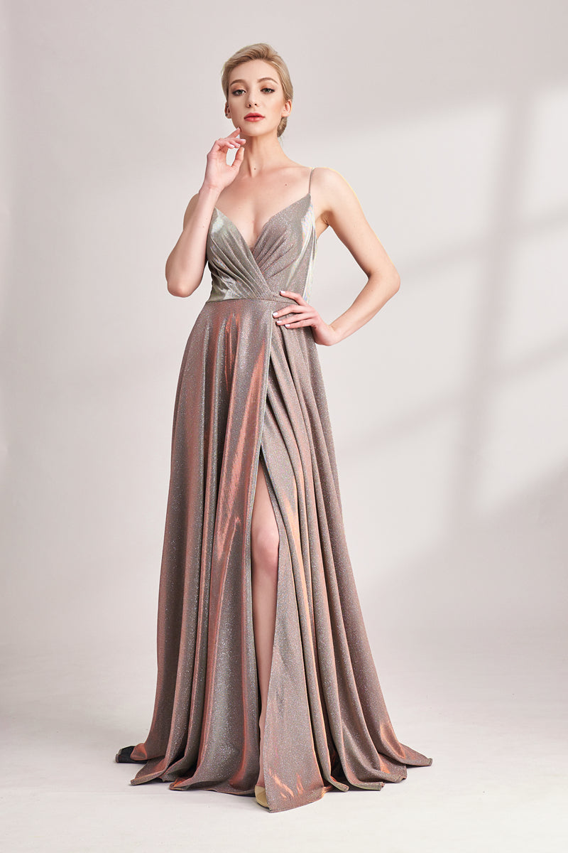 This is an elegant evening gown, floor-length, silver and rose gold color, draped fabric, deep V-neck, one leg exposed, blonde hair, short bob, fair skin, standing pose, hand on hip, other hand touching face, neutral expression, soft lighting, minimalistic background, white backdrop, shadows on the wall, sophisticated, glamorous, fashion, high-fashion photography, studio shot, full body, front view