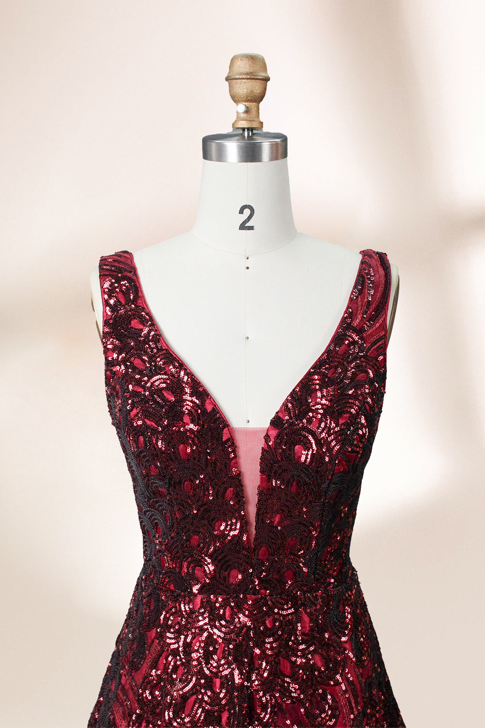 A photograph of a model dress on a dress form. The dress is a sleeveless, deep V-neck gown with a plunging neckline. It features a rich, deep red color with intricate, swirling black and red patterns, giving it a luxurious and elegant appearance. The background is a soft, neutral tone, with gentle shadows cast on the dress form.32625.3