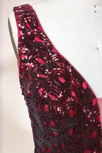 A photograph of a model dress on a dress form. The dress is a sleeveless, deep V-neck gown with a plunging neckline. It features a rich, deep red color with intricate, swirling black and red patterns, giving it a luxurious and elegant appearance. The background is a soft, neutral tone, with gentle shadows cast on the dress form.