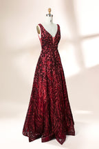 A photograph of a model dress on a dress form. The dress is a sleeveless, deep V-neck gown with a plunging neckline. It features a rich, deep red color with intricate, swirling black and red patterns, giving it a luxurious and elegant appearance. The background is a soft, neutral tone, with gentle shadows cast on the dress form.32625.6