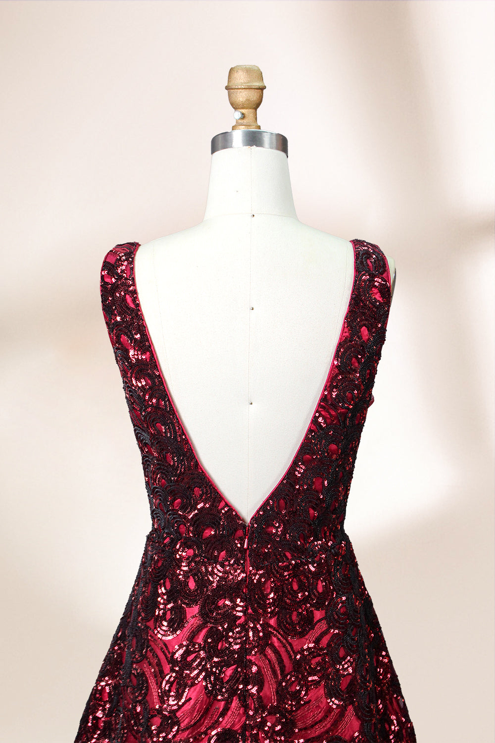 A photograph of a model dress on a dress form. The dress is a sleeveless, deep V-neck gown with a plunging neckline. It features a rich, deep red color with intricate, swirling black and red patterns, giving it a luxurious and elegant appearance. The background is a soft, neutral tone, with gentle shadows cast on the dress form.32625.7