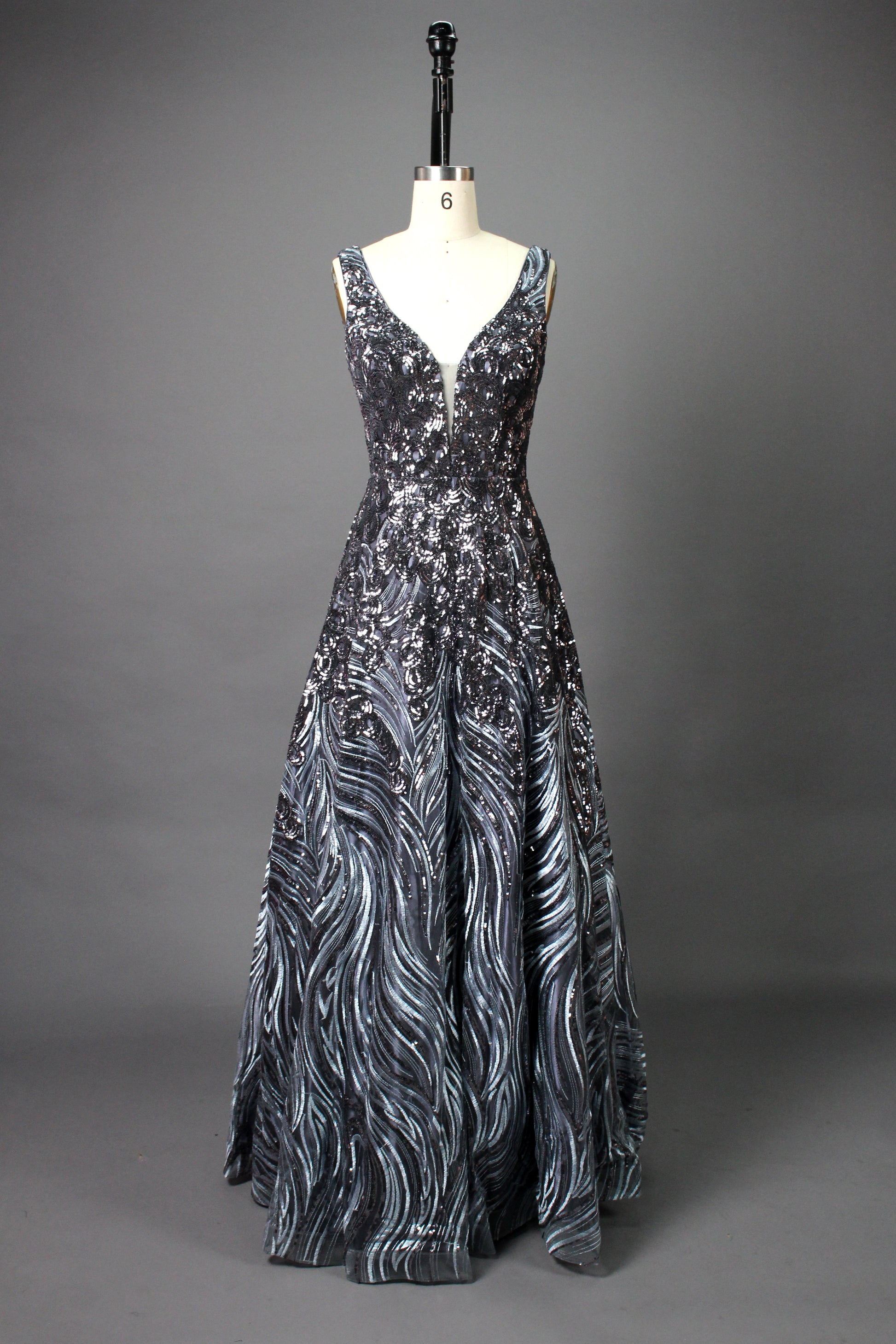 A photograph of a model dress on a dress form. The dress is a sleeveless, deep V-neck gown with a plunging neckline. It features a rich, deep red color with intricate, swirling black and red patterns, giving it a luxurious and elegant appearance. The background is a soft, neutral tone, with gentle shadows cast on the dress form.