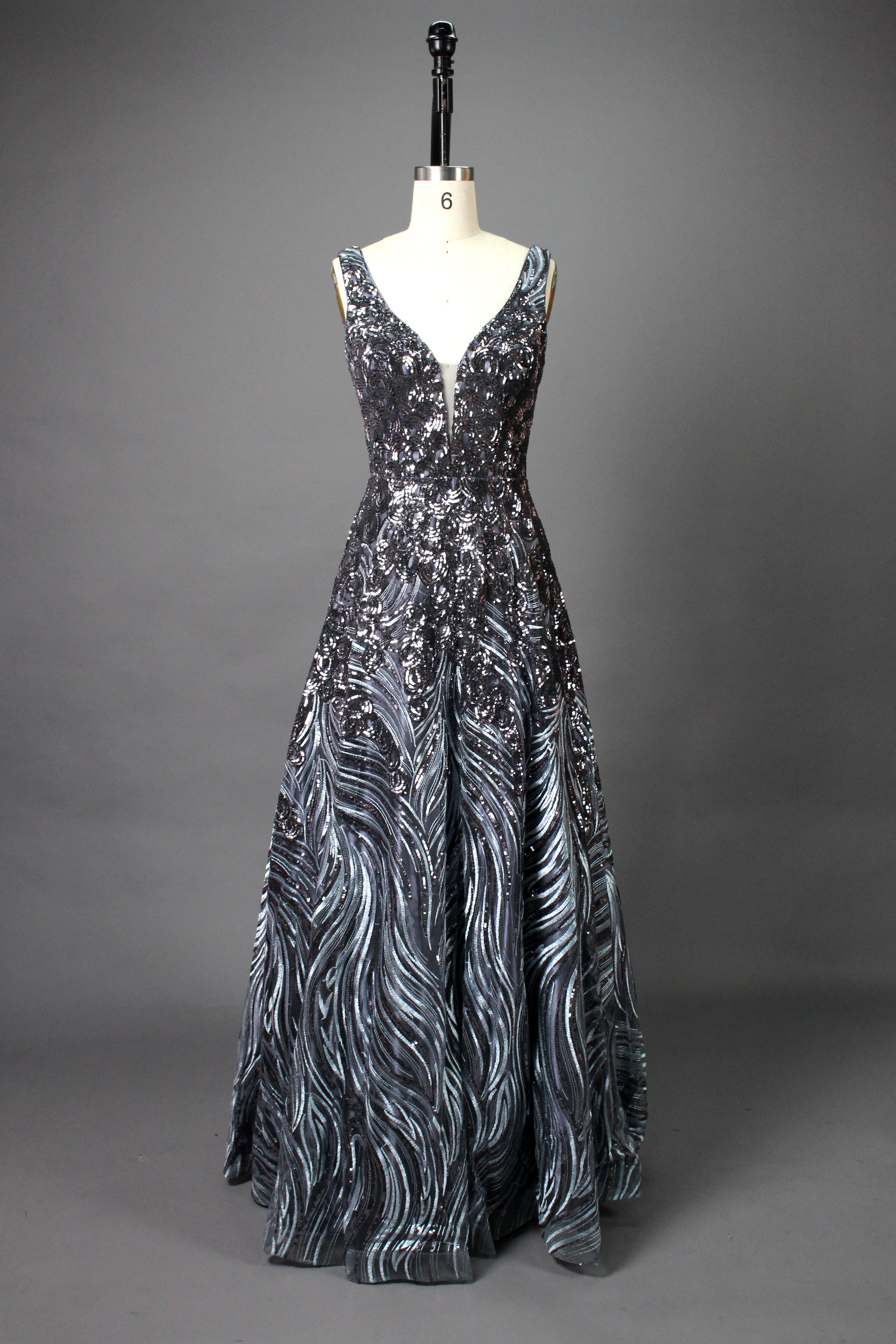 A photograph of a model dress on a dress form. The dress is a sleeveless, deep V-neck gown with a plunging neckline. It features a rich, deep red color with intricate, swirling black and red patterns, giving it a luxurious and elegant appearance. The background is a soft, neutral tone, with gentle shadows cast on the dress form.