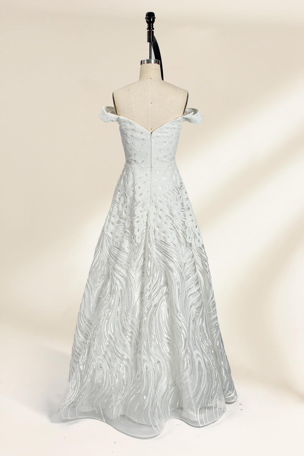 Photograph of a white, off-the-shoulder wedding gown displayed on a black dress form against a cream backdrop. The gown features intricate, swirling floral lace embroidery with a fitted bodice and a full, flared skirt, exuding elegance and sophistication. The dress form is centered, highlighting the gown's delicate detailing and flowing texture.32625b.2