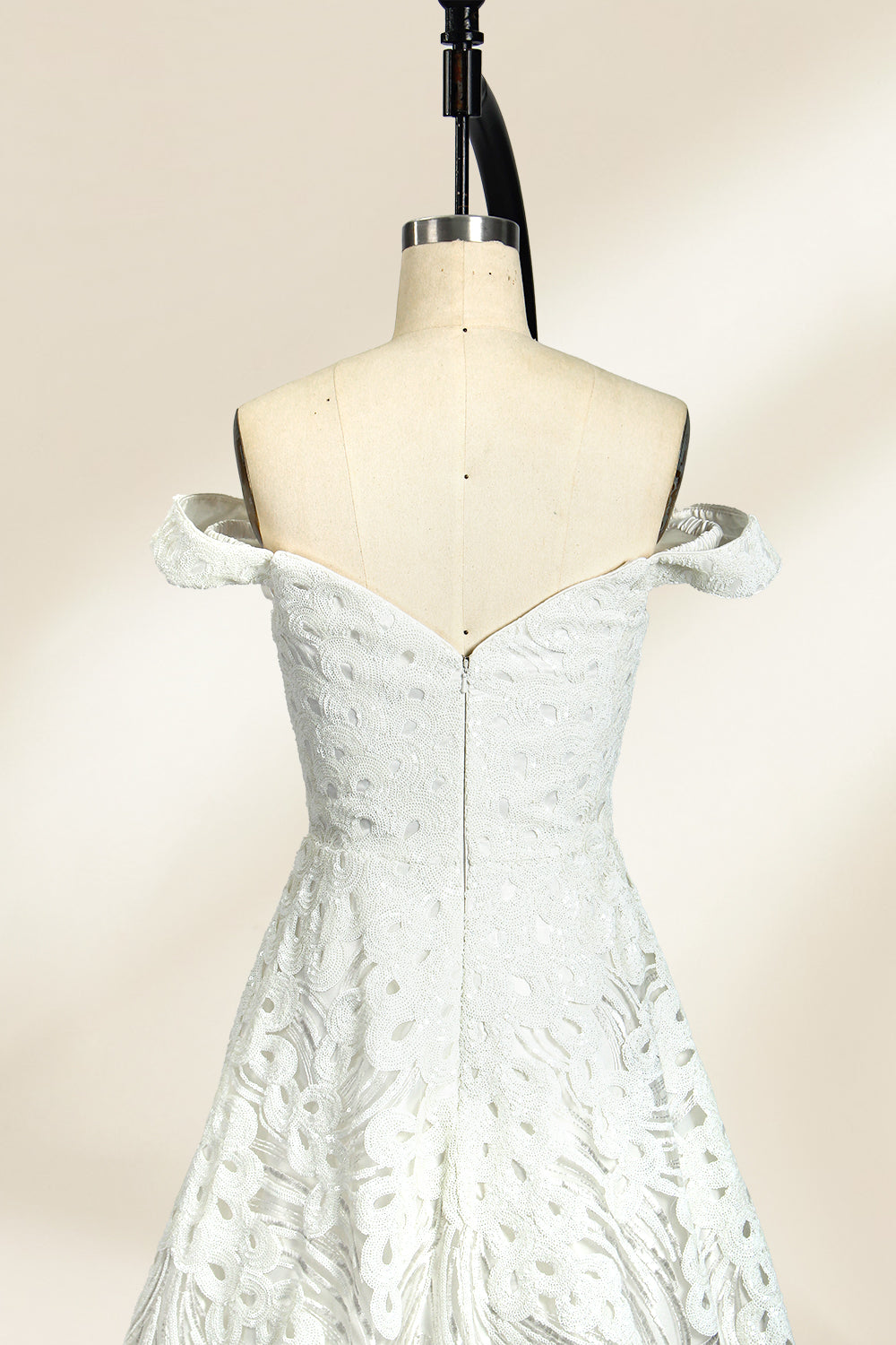 Photograph of a white, off-the-shoulder wedding gown displayed on a black dress form against a cream backdrop. The gown features intricate, swirling floral lace embroidery with a fitted bodice and a full, flared skirt, exuding elegance and sophistication. The dress form is centered, highlighting the gown's delicate detailing and flowing texture.32625b.4