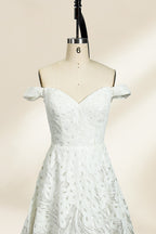 Photograph of a white, off-the-shoulder wedding gown displayed on a black dress form against a cream backdrop. The gown features intricate, swirling floral lace embroidery with a fitted bodice and a full, flared skirt, exuding elegance and sophistication. The dress form is centered, highlighting the gown's delicate detailing and flowing texture.32625b.5
