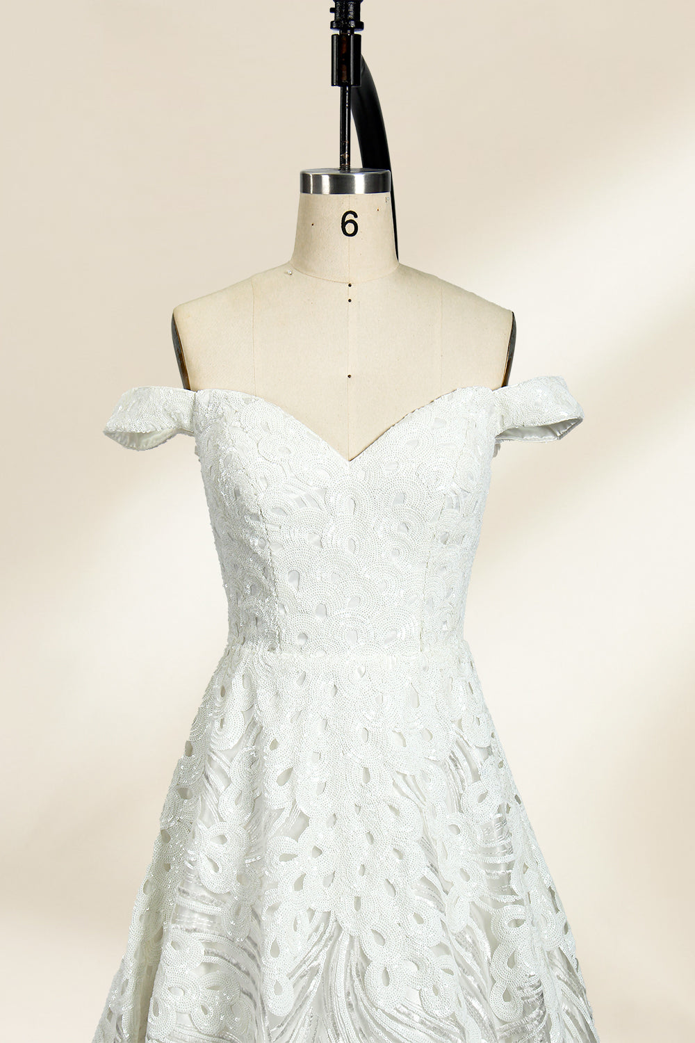 Photograph of a white, off-the-shoulder wedding gown displayed on a black dress form against a cream backdrop. The gown features intricate, swirling floral lace embroidery with a fitted bodice and a full, flared skirt, exuding elegance and sophistication. The dress form is centered, highlighting the gown's delicate detailing and flowing texture.32625b.5
