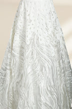 Photograph of a white, off-the-shoulder wedding gown displayed on a black dress form against a cream backdrop. The gown features intricate, swirling floral lace embroidery with a fitted bodice and a full, flared skirt, exuding elegance and sophistication. The dress form is centered, highlighting the gown's delicate detailing and flowing texture.32625b.6