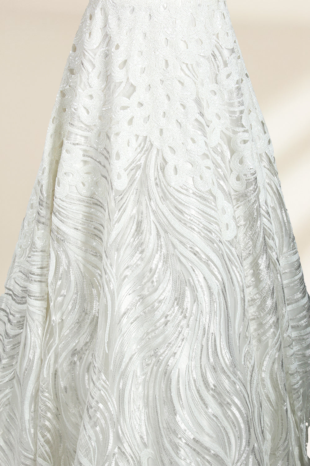Photograph of a white, off-the-shoulder wedding gown displayed on a black dress form against a cream backdrop. The gown features intricate, swirling floral lace embroidery with a fitted bodice and a full, flared skirt, exuding elegance and sophistication. The dress form is centered, highlighting the gown's delicate detailing and flowing texture.32625b.6
