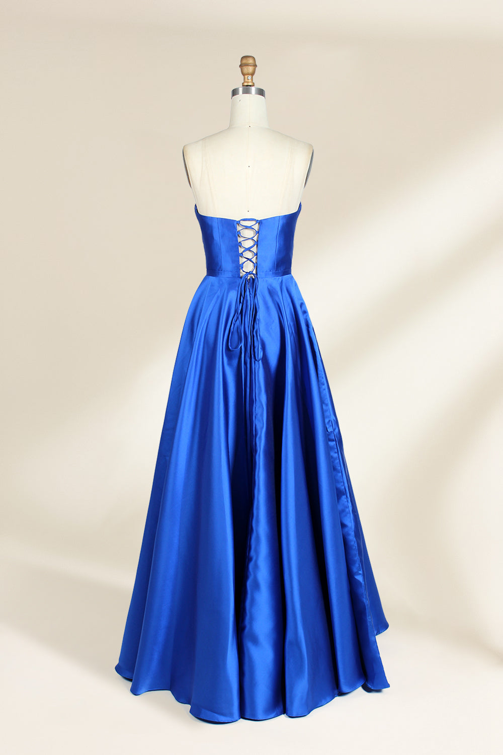 A photograph of a mannequin wearing a strapless, floor-length blue satin gown with a sweetheart neckline. The dress features a fitted bodice and a voluminous skirt. The mannequin stands against a plain, cream-colored background, highlighting the dress's elegant, flowing fabric and vibrant color.32638.4
