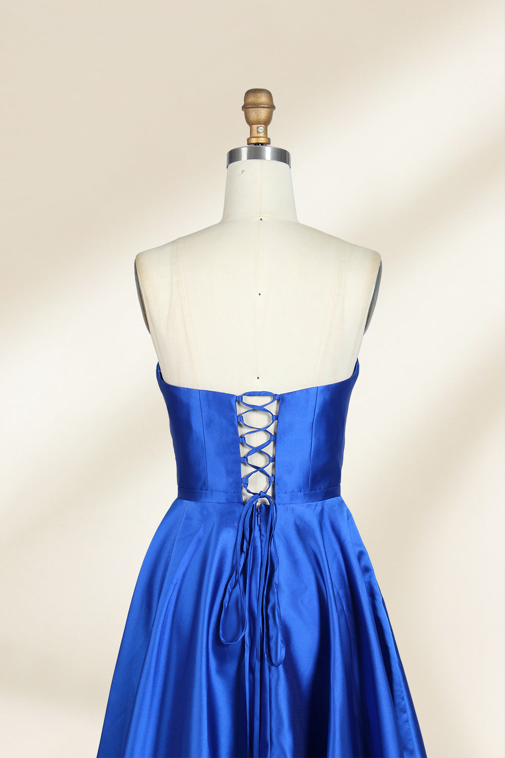 A photograph of a mannequin wearing a strapless, floor-length blue satin gown with a sweetheart neckline. The dress features a fitted bodice and a voluminous skirt. The mannequin stands against a plain, cream-colored background, highlighting the dress's elegant, flowing fabric and vibrant color.32638.5