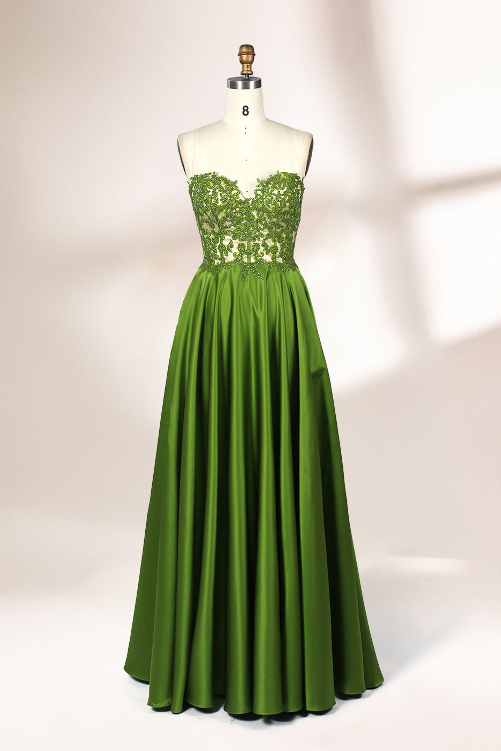 Photograph of an elegant, strapless gown displayed on a mannequin. The gown features a green, satin bodice adorned with intricate lace detailing and a full, floor-length skirt. The background is a soft, neutral gradient, enhancing the gown's vibrant green color. The mannequin is positioned centrally, with the gown's luxurious texture and refined craftsmanship prominently showcased.32639.1
