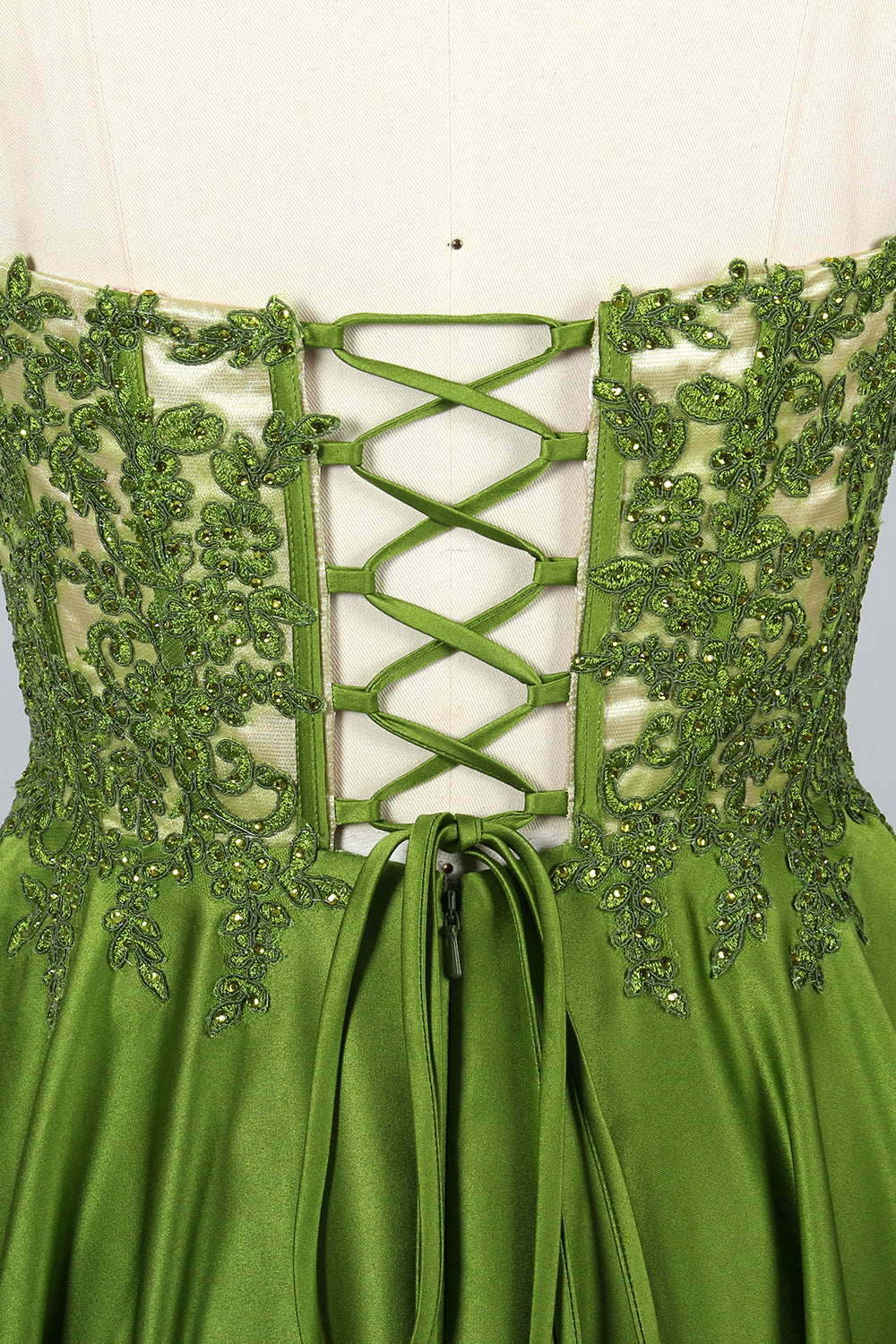 Photograph of an elegant, strapless gown displayed on a mannequin. The gown features a green, satin bodice adorned with intricate lace detailing and a full, floor-length skirt. The background is a soft, neutral gradient, enhancing the gown's vibrant green color. The mannequin is positioned centrally, with the gown's luxurious texture and refined craftsmanship prominently showcased.32639.3