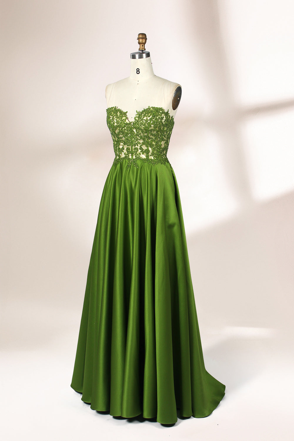 Photograph of an elegant, strapless gown displayed on a mannequin. The gown features a green, satin bodice adorned with intricate lace detailing and a full, floor-length skirt. The background is a soft, neutral gradient, enhancing the gown's vibrant green color. The mannequin is positioned centrally, with the gown's luxurious texture and refined craftsmanship prominently showcased.32639.5