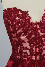 Photograph of an elegant, strapless gown displayed on a mannequin. The gown features a green, satin bodice adorned with intricate lace detailing and a full, floor-length skirt. The background is a soft, neutral gradient, enhancing the gown's vibrant green color. The mannequin is positioned centrally, with the gown's luxurious texture and refined craftsmanship prominently showcased.
