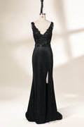 A photograph of a black, floor-length evening gown with a deep V-neck and lace detailing, featuring a thigh-high slit on the left side. The dress is displayed on a white mannequin with a black stand against a soft, beige background with diffused lighting creating gentle shadows. The gown exudes elegance and sophistication.32645.1