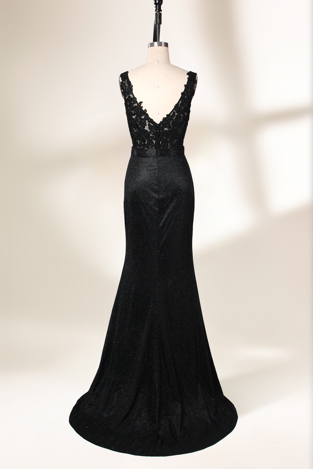 A photograph of a black, floor-length evening gown with a deep V-neck and lace detailing, featuring a thigh-high slit on the left side. The dress is displayed on a white mannequin with a black stand against a soft, beige background with diffused lighting creating gentle shadows. The gown exudes elegance and sophistication.32645.2