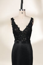 A photograph of a black, floor-length evening gown with a deep V-neck and lace detailing, featuring a thigh-high slit on the left side. The dress is displayed on a white mannequin with a black stand against a soft, beige background with diffused lighting creating gentle shadows. The gown exudes elegance and sophistication.32645.5
