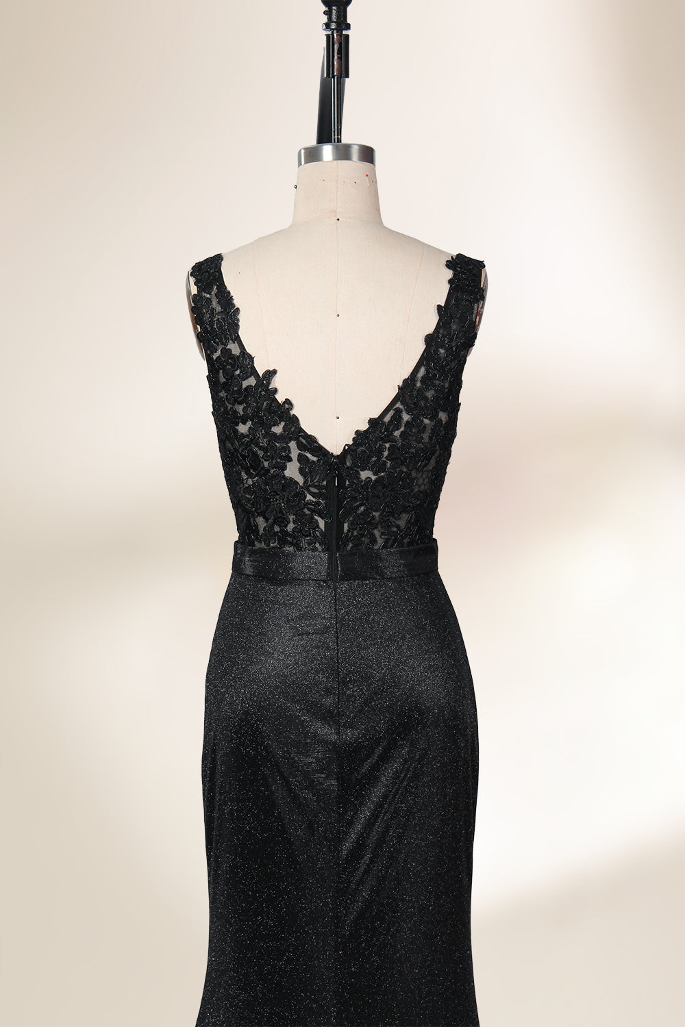 A photograph of a black, floor-length evening gown with a deep V-neck and lace detailing, featuring a thigh-high slit on the left side. The dress is displayed on a white mannequin with a black stand against a soft, beige background with diffused lighting creating gentle shadows. The gown exudes elegance and sophistication.32645.6