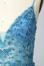 A photograph of a mannequin wearing a floor-length, blue evening gown. The dress features a deep V-neckline adorned with intricate beading, a fitted bodice, and a flowing, high slit skirt. The background is a plain, light beige color, highlighting the gown's elegant design and delicate textures.32656.03