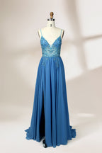 A photograph of a mannequin wearing a floor-length, blue evening gown. The dress features a deep V-neckline adorned with intricate beading, a fitted bodice, and a flowing, high slit skirt. The background is a plain, light beige color, highlighting the gown's elegant design and delicate textures.32656.1
