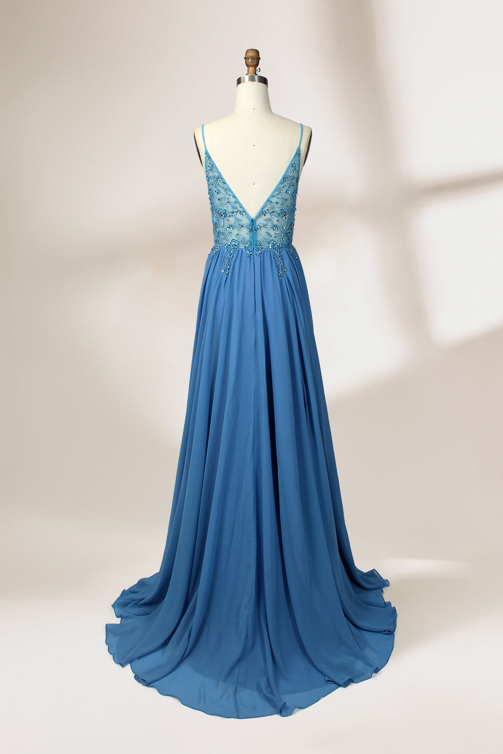 A photograph of a mannequin wearing a floor-length, blue evening gown. The dress features a deep V-neckline adorned with intricate beading, a fitted bodice, and a flowing, high slit skirt. The background is a plain, light beige color, highlighting the gown's elegant design and delicate textures.32656.2