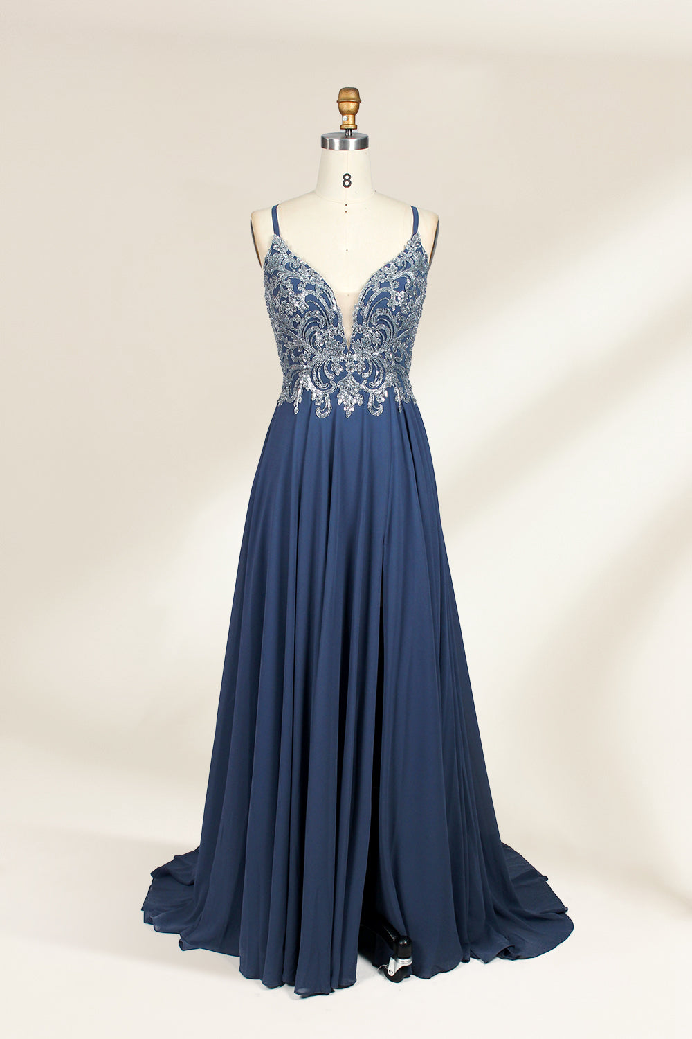 Photograph of a mannequin showcasing an elegant, floor-length evening gown. The gown features a deep V-neckline adorned with intricate blue floral embroidery, transitioning into a flowing, dark blue chiffon skirt. The mannequin stands against a plain, cream-colored backdrop. The dress exudes sophistication and luxury, perfect for formal events.01