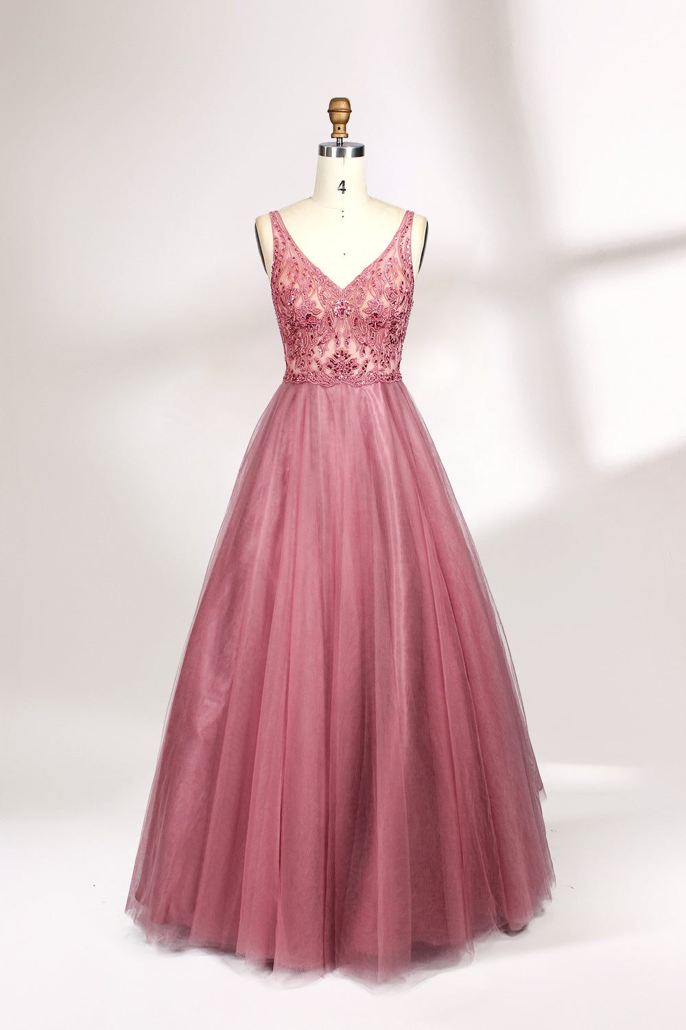 Photograph of a mannequin showcasing a floor-length, sleeveless, pink tulle gown with intricate lace detailing on the bodice and neckline. The gown features a fitted waist and flares out into a voluminous skirt, creating a ballerina-style silhouette. The mannequin stands against a plain white background with soft, diffused lighting casting subtle shadows.01