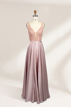 Photograph of a sleeveless, floor-length evening gown displayed on a dress form. The gown features a deep V-neckline adorned with intricate lace detailing and a sheer, blush pink fabric that flows into a smooth, satin skirt. The dress form is positioned against a plain, light beige background, emphasizing the gown's elegant design.01