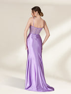 Photograph of a slender, light-skinned woman with brunette hair in a bun, wearing a strapless, lavender satin gown with intricate lace detailing on the back. The gown has a fitted bodice and a flowing, floor-length skirt. She stands against a plain, cream-colored background, with soft shadows adding depth. The gown's texture appears smooth and luxurious. The overall aesthetic is elegant and sophisticated.32738-02