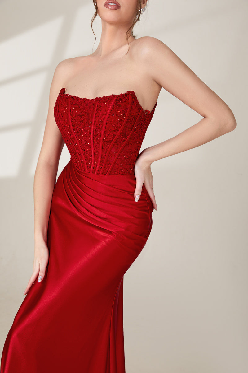 photograph of a beautiful woman, standing in front of a plain white background, wearing a stunning red strapless gown with a high slit, intricate lace detailing on the bodice, long flowing skirt, elegant black high heels, long legs, brunette hair styled in an updo, confident pose, soft lighting, shadows on the wall, modern fashion, sophisticated, glamorous, high fashion, elegant attire