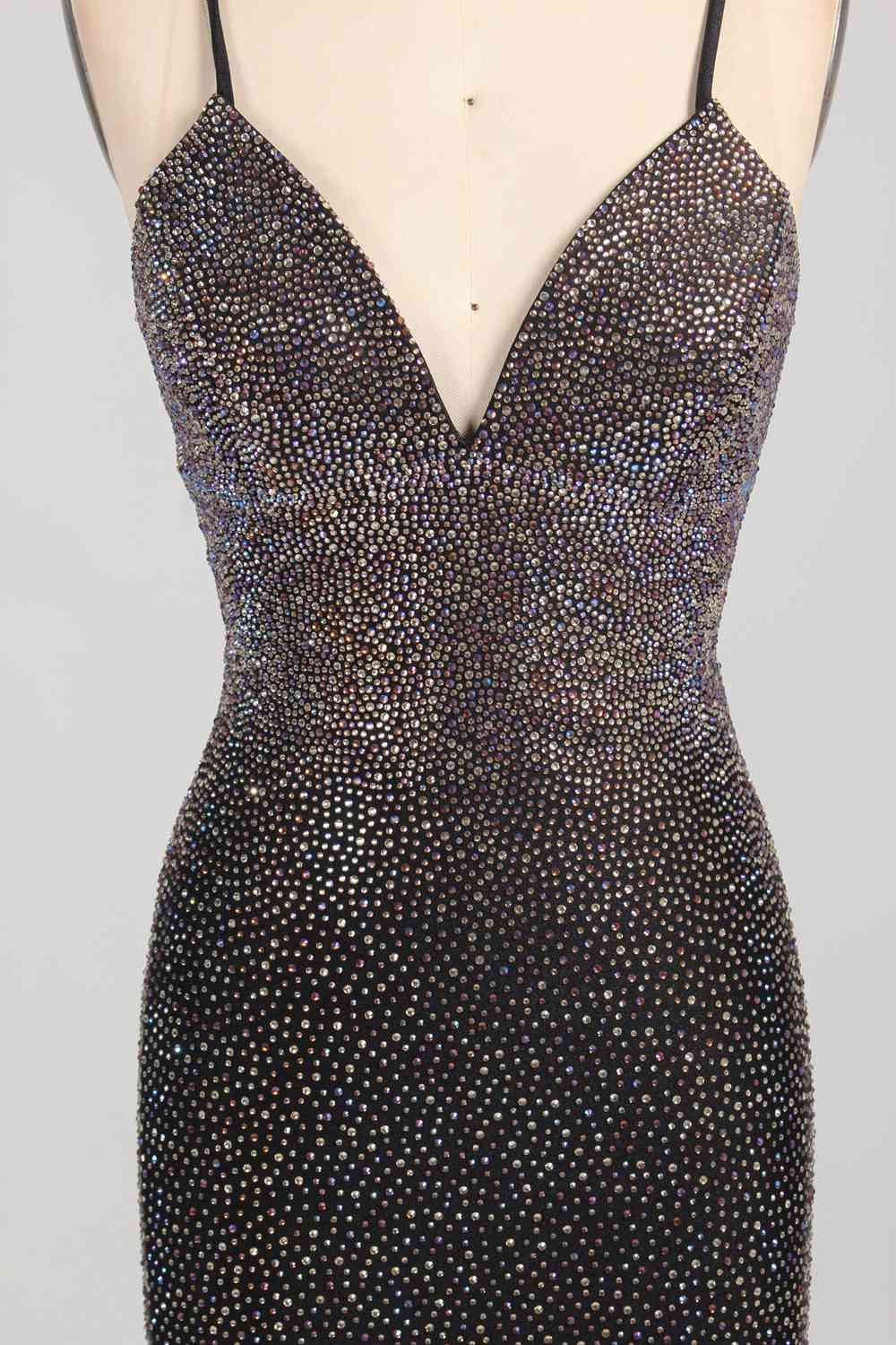 Photograph of a woman's torso wearing a form-fitting, black sequined dress with a deep V-neckline and spaghetti straps. The dress sparkles with a mix of small, shimmering sequins, creating a luxurious, textured appearance. The woman's skin tone is light, and her arms are raised above her head, slightly visible at the top of the image. The background is a plain, light grey, ensuring the focus remains on the dress. The overall style is elegant and glamorous, suitable for formal occasions.
