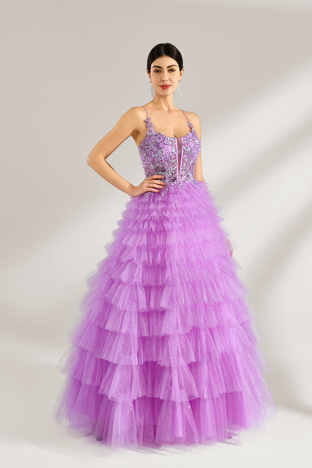 A woman with sleek dark hair and a poised stance wears a light - purple tulle gown. It has thin straps, a lace - detailed bodice, and a tiered, voluminous skirt. Paired with understated heels, the outfit radiates elegance, perfect for formal events like galas or proms.1