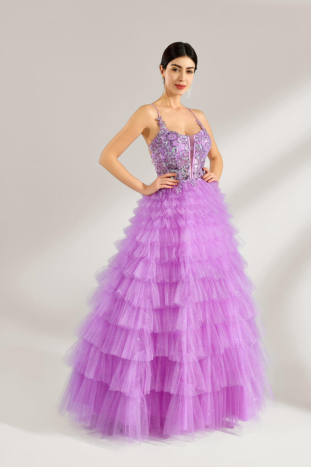 A woman with sleek dark hair and a poised stance wears a light - purple tulle gown. It has thin straps, a lace - detailed bodice, and a tiered, voluminous skirt. Paired with understated heels, the outfit radiates elegance, perfect for formal events like galas or proms.2
