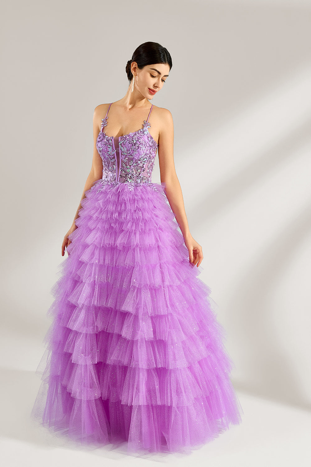 A woman with sleek dark hair and a poised stance wears a light - purple tulle gown. It has thin straps, a lace - detailed bodice, and a tiered, voluminous skirt. Paired with understated heels, the outfit radiates elegance, perfect for formal events like galas or proms.3