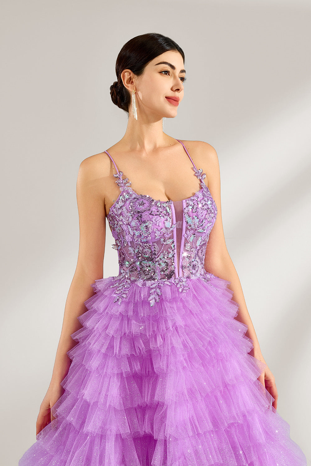 A woman with sleek dark hair and a poised stance wears a light - purple tulle gown. It has thin straps, a lace - detailed bodice, and a tiered, voluminous skirt. Paired with understated heels, the outfit radiates elegance, perfect for formal events like galas or proms.5