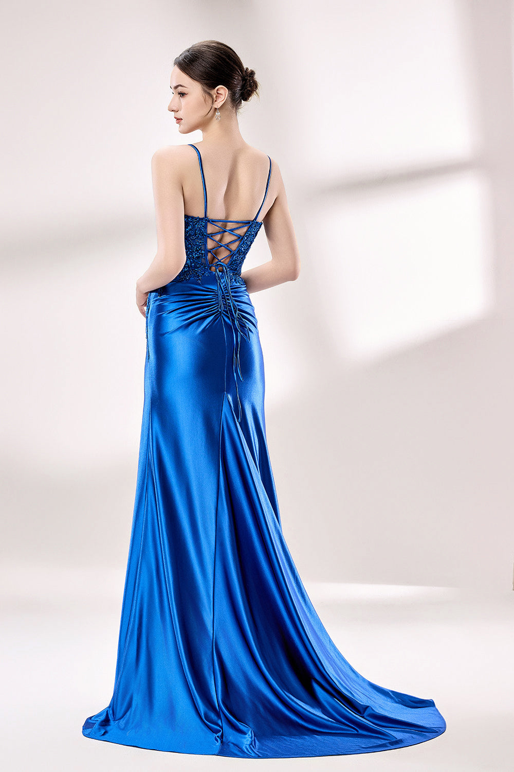 photograph of a beautiful woman wearing a stunning royal blue evening gown with a thigh-high slit, intricate lace detailing on the bodice, elegant design, long sleeves, slim fit, standing in a studio with soft lighting, white background, delicate jewelry, dark hair styled in a sleek updo, confident pose, graceful, sophisticated, fashion photography, high-quality, luxurious, formal attire, glamorous.33028-02